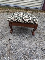 Full view of antique foot stool showing wooden frame and cabriole legs, with patterned upholstered cushion on top.