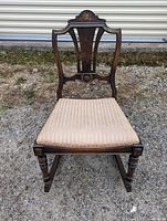 Front view revealing carved wooden backrest and upholstered seat with turned legs and rockers.