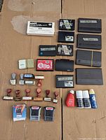 Top view photo showing a variety of rubber stamps including rotary date stamps, self-inking stamps, wooden handled stamps, and multiple ink pads mostly black and red.
