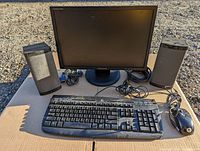Full set including Samsung monitor, Logitech keyboard, wired mouse, and two speakers on cardboard outdoors