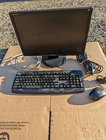 Front view of Samsung LCD monitor with HP keyboard and mouse on cardboard surface outdoors.