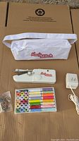Handy Stitch sewing kit contents arranged on cardboard including sewing tool, full set of threads, charger, and white carrying bag