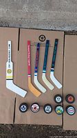 Full view of the five mini goalie sticks and eight hockey pucks laid out on cardboard.