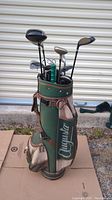 Full side view of the Augusta golf bag filled with clubs, showing leather strap and pockets, outdoors on ground.