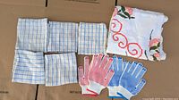 Photo showing five checkered dishtowels, two pairs of grip-studded gloves (red and blue), and a folded retro-style embroidered tablecloth.