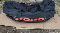 Black KOHO hockey bag laid flat, showing orange logo on the side with visible wear.