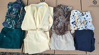 Four sets of ladies dresswear including blouses and matching skirts or pants, laid out flat on cardboard