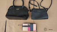 Photo showing two black purses and one multicolor Kate Spade wallet laid on cardboard.
