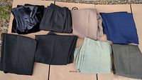 Lot of eight ladies slacks and pants folded and displayed on cardboard outdoors, showing multiple colors and styles, mainly solid colors with some elastic waistbands visible.