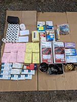 Full lot showing all grouped office supplies including rolls, message books, clips, and pads on cardboard surface.