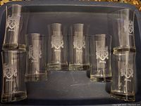 Eight tall clear glasses arranged in a plastic container, each with the Steacy crest etched on the front