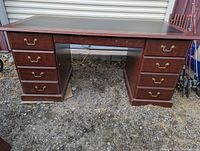 Full front view of the red wood colored office desk with black surface, showing two sets of pedestal drawers and the modesty panel below the desktop.