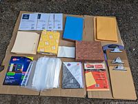 Top view of assorted office supplies arranged on cardboard including paper pads, envelopes, clipboards, folders, and poly sheets.
