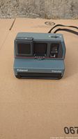 Front view of gray Polaroid Impulse camera showing lens, flash, and front cover with Polaroid impulse branding.