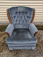 Front view of blue cushioned chair with tufted backrest, wooden accents on armrests, and pleated skirt base.