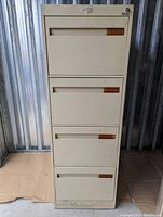 Front view of tall beige 4-drawer filing cabinet showing recessed drawer handles and lock with keyhole at top right.