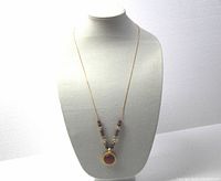 Full view of necklace on display bust showing gold toned chain and round pendant with beads.