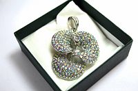 Pendant viewed inside black jewelry box on white cushion, showing full top and front view details of rhinestone encrusted circular shapes.