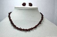 Full view of garnet chip necklace displayed on neck stand along with matching flower design earrings.