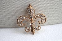 Front angled view of gold tone fleur-de-lis brooch highlighting rhinestones and faux pearls on one side.