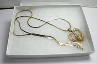 Gold tone heart pendant necklace with rhinestones on a 24 inch chain, displayed inside a white box on white padding.