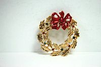 Front view of gold tone wreath brooch showing detailed leaves, red and green rhinestones, and bright red enameled bow