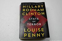 Front cover of the book 'State of Terror' by Hillary Rodham Clinton and Louise Penny, showing the title and authors' names in bold text with a red diamond design element.