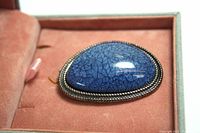 Close-up view of the blue pendant showing the textured, glossy finish and twisted silver-tone bezel setting, inside pink velvet-lined box.