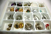 Plastic tray holding 17 pairs of assorted earrings featuring different colors, sizes and styles including carved roses, hoops, clip-ons, silver and gold-tone finishes.