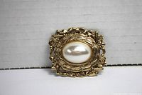 Front view of gold tone floral brooch with large oval faux pearl center.
