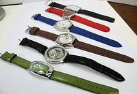 Top view of six wristwatches lined up horizontally showing various strap colors and dial shapes.