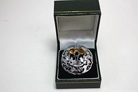 Silver-tone round brooch with intricate Scottish theme including leaves and thistle, set with two amber gem stones, inside a dark green gift box with satin lining.