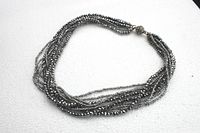 Photo of the necklace laid flat on a light background showing the fullness and length of the strands and the magnetic bead clasp.