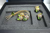 Full jewelry set view in black foam-lined gift box, showing brooch and clip earrings with green stones and gold-tone finish.