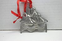 Front view of the pewter ship Christmas ornament with red ribbon, displaying the inscription 'On Christmas Day In The Morning.'