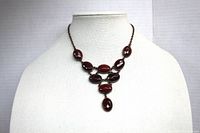 Full view of the vintage red stone necklace displayed on a white bust showing the triangular arrangement of the stones in copper-tone settings.