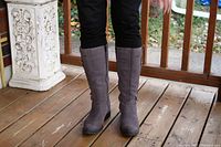 Front view of both brown mid-calf boots worn by a model, showing length and color on wooden porch.