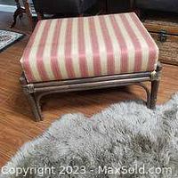 Photo showing one rattan foot stool with red and cream striped upholstery on cushion top, placed on wooden floor with furniture visible in background.