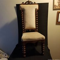 Front view of antique barley twist chair showing detailed carved wooden frame and cream upholstery on backrest and seat.
