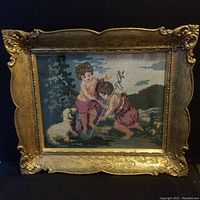 Front view of framed needlework tapestry depicting two children and a dog in a pastoral scene in gold ornate frame