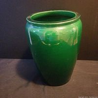 Full view of the antique grass green glazed ceramic vase, upright on a black surface, showing its glossy finish and shape.