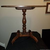 Full side view of antique wooden side table showing round top, turned pedestal, and four legs.