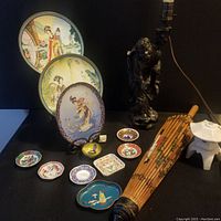 Full view of Asian decorative items including plates, figurine lamp, parasol, small dishes, and incense holder.