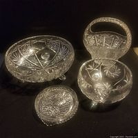 Four pieces of vintage cut crystal displayed on black background including bowl, basket, footed bowl, and small dish.