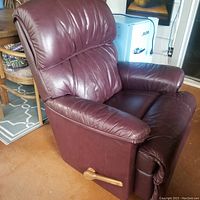 Side angle showing burgundy leather recliner with plush padding and wooden recline lever.