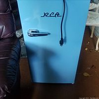 Front view of vintage blue RCA bar fridge with chrome handle and power cord visible.