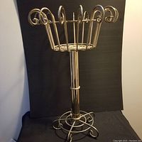 Front view of the brass plant stand showing its decorative curled accents and basket top with a round base.