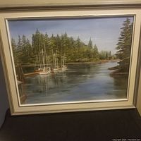 Full view of the oil painting featuring the scenic lakeside with sailboats and pine trees, framed and displayed on a flat surface.