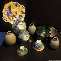 Full lot view showing seven pottery items including three beige vases, a large floral bowl, a decorative yellow and purple scalloped edge plate, and three small colorful patterned bowls.
