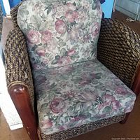 Front angled view of rattan braided wicker armchair with floral fabric cushions and wood armrest accents.